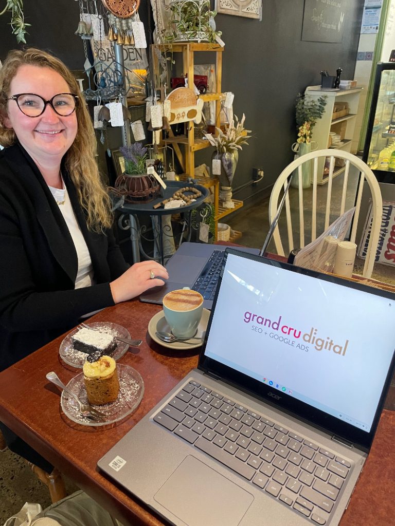 Casey-smiling-with-2-cakes-2-laptops-and-a-chai-latte-at-Fine-aromas