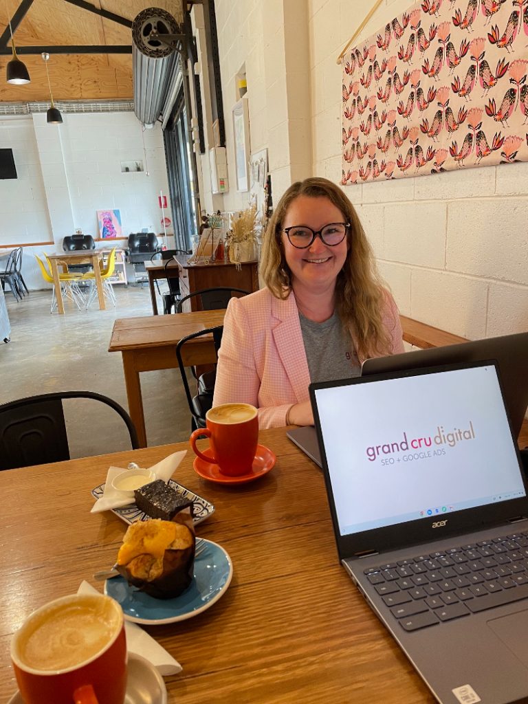 Two coffees and cakes with a GCD laptop and Casey smiling at Hello Birdie Cafe